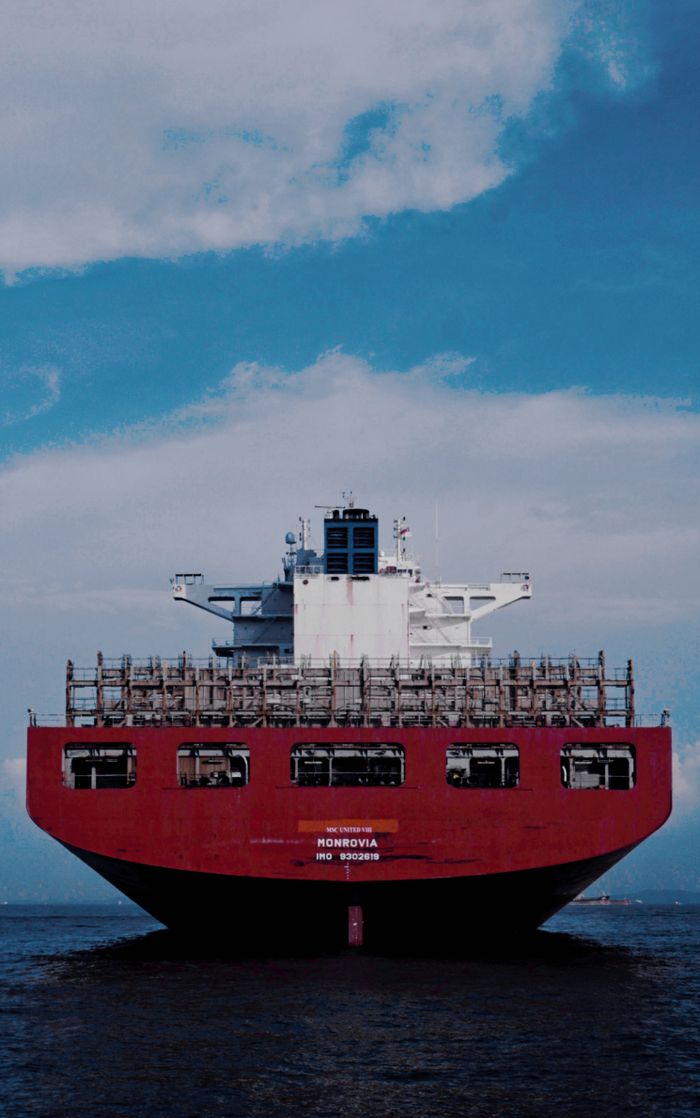 our-services-1 Large red cargo ship transporting goods across the ocean under a bright blue sky.