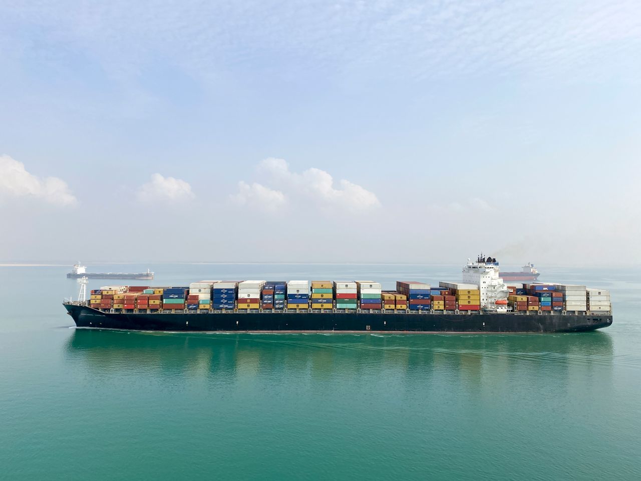 contact-img Aerial view of a large cargo ship filled with containers sailing on a calm sea under a clear sky.